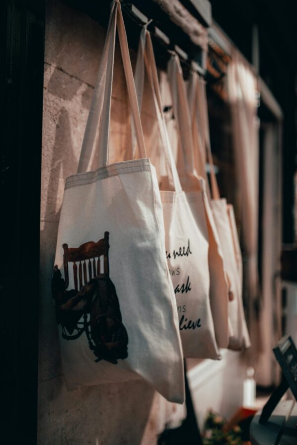 Close-up of canvas tote bags hanging on a rack in a warmly lit store interior.